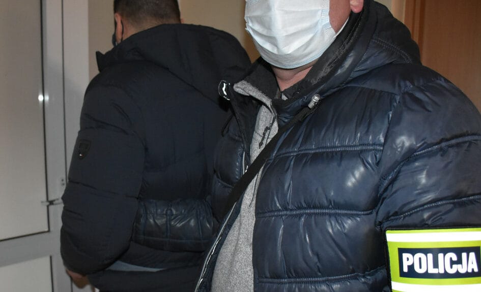 Policjant aresztujący podejrzanego. Widoczna opaska POLICJI.