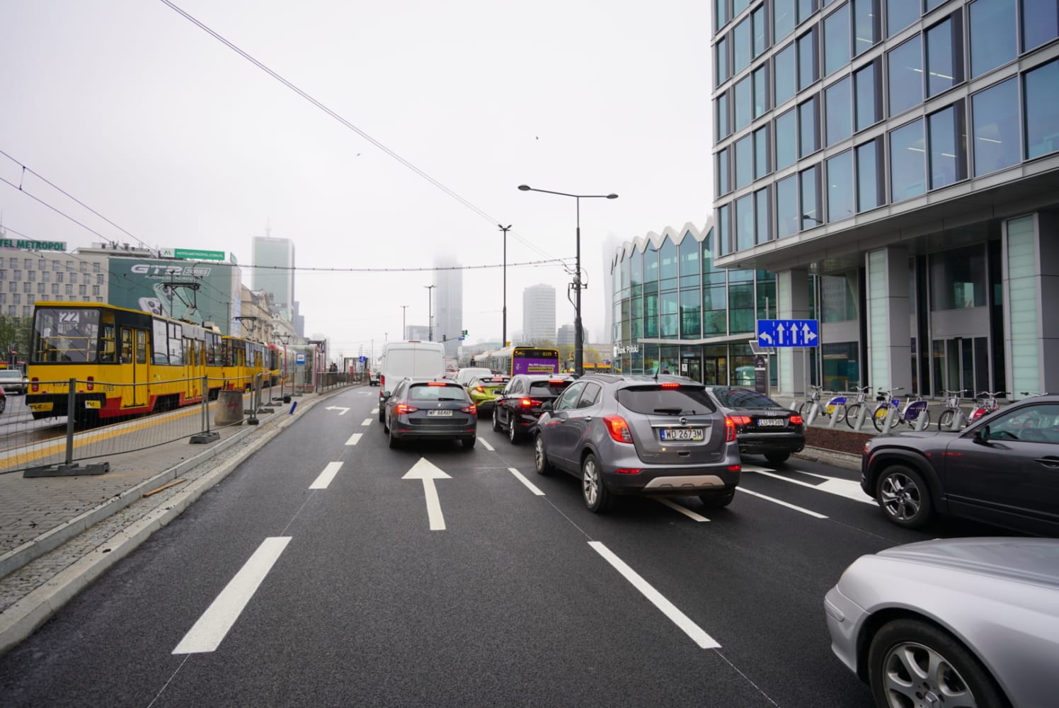 Scena uliczna miasta z tramwajami, samochodami i nowoczesnymi budynkami.