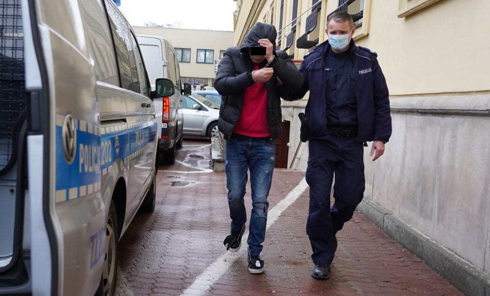 Policjant eskortujący podejrzanego w kajdankach.