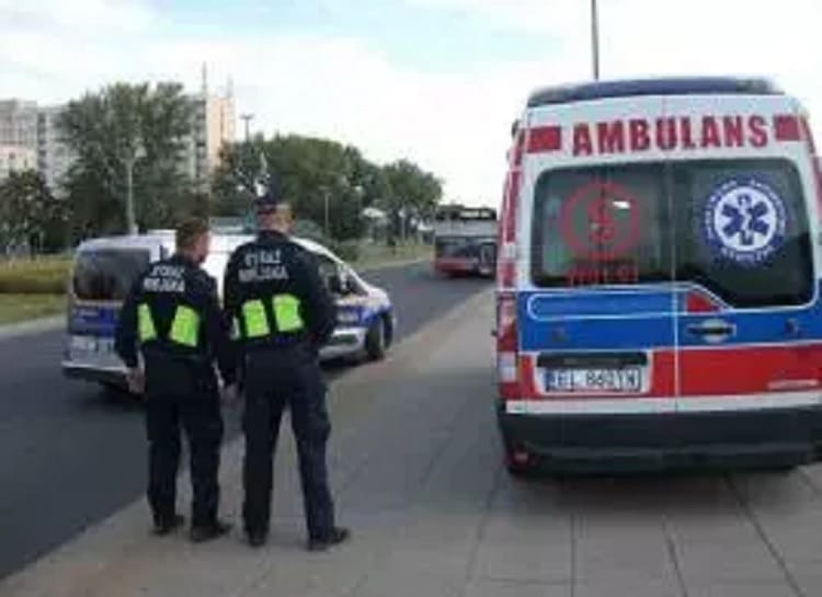 Dwóch polskich policjantów stoi obok karetki pogotowia i radiowozu na miejscu zdarzenia.
