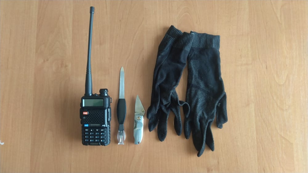 Czarne rękawiczki, scyzoryk, pilnik do paznokci i radiotelefon na drewnie