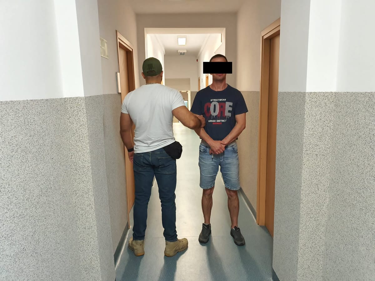 Policjant eskortujący podejrzanego korytarzem szpitalnym.