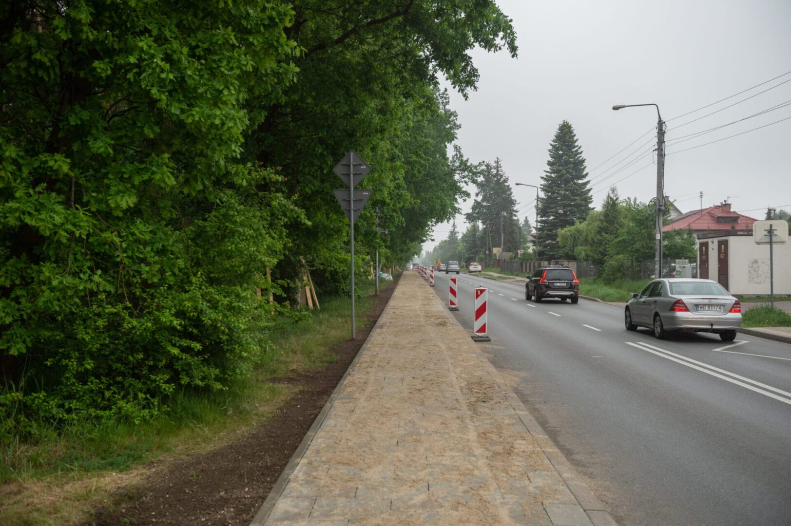 Nowo wybudowany chodnik i jezdnia, po której jeżdżą samochody. Budowa drogi w toku.