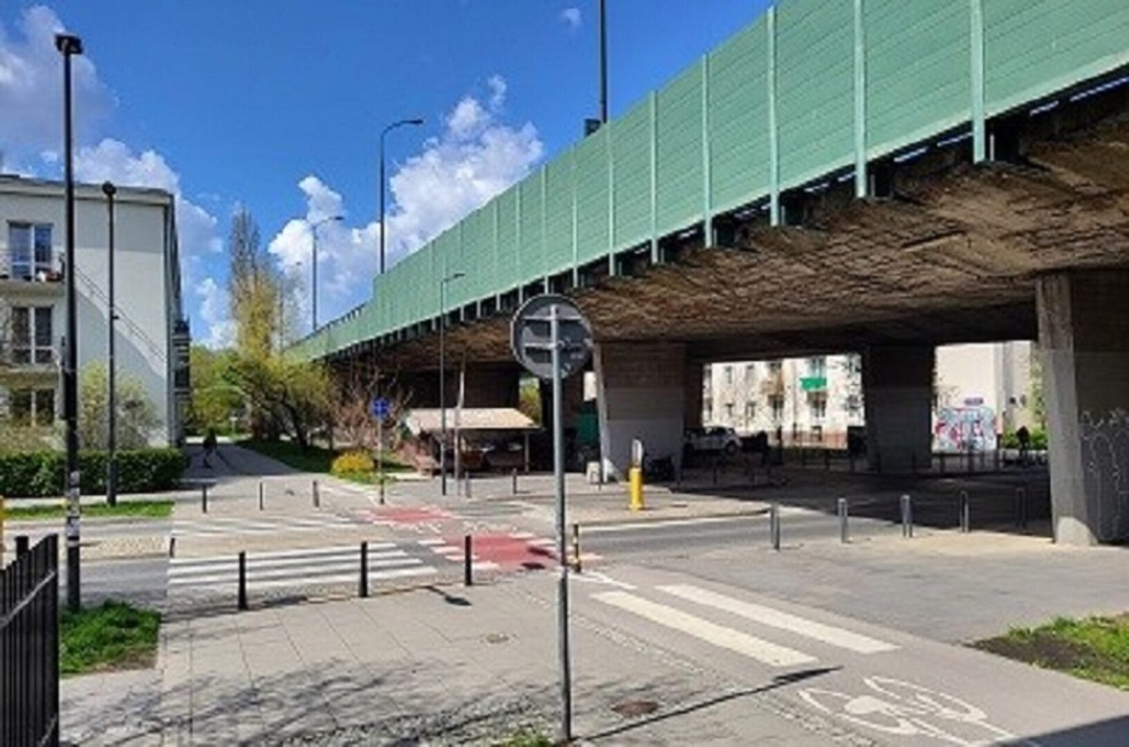 Ścieżka dla pieszych i rowerzystów pod wiaduktem drogowym z ekranem akustycznym.