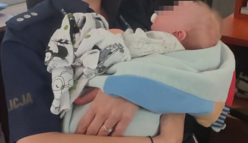 Policjant trzyma na rękach śpiące dziecko, owinięte w kolorowy kocyk.