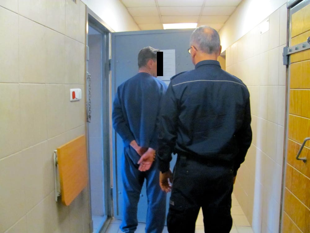 Korytarz więzienny ze strażnikiem eskortującym więźnia.