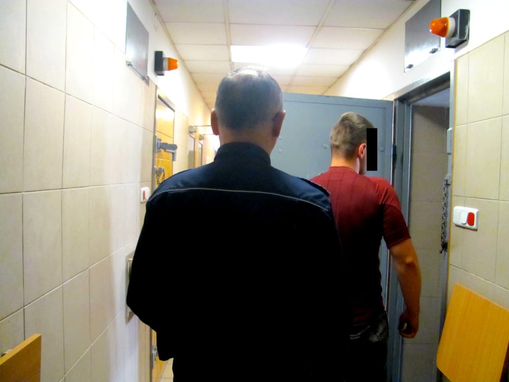 Policjant eskortujący więźnia korytarzem.