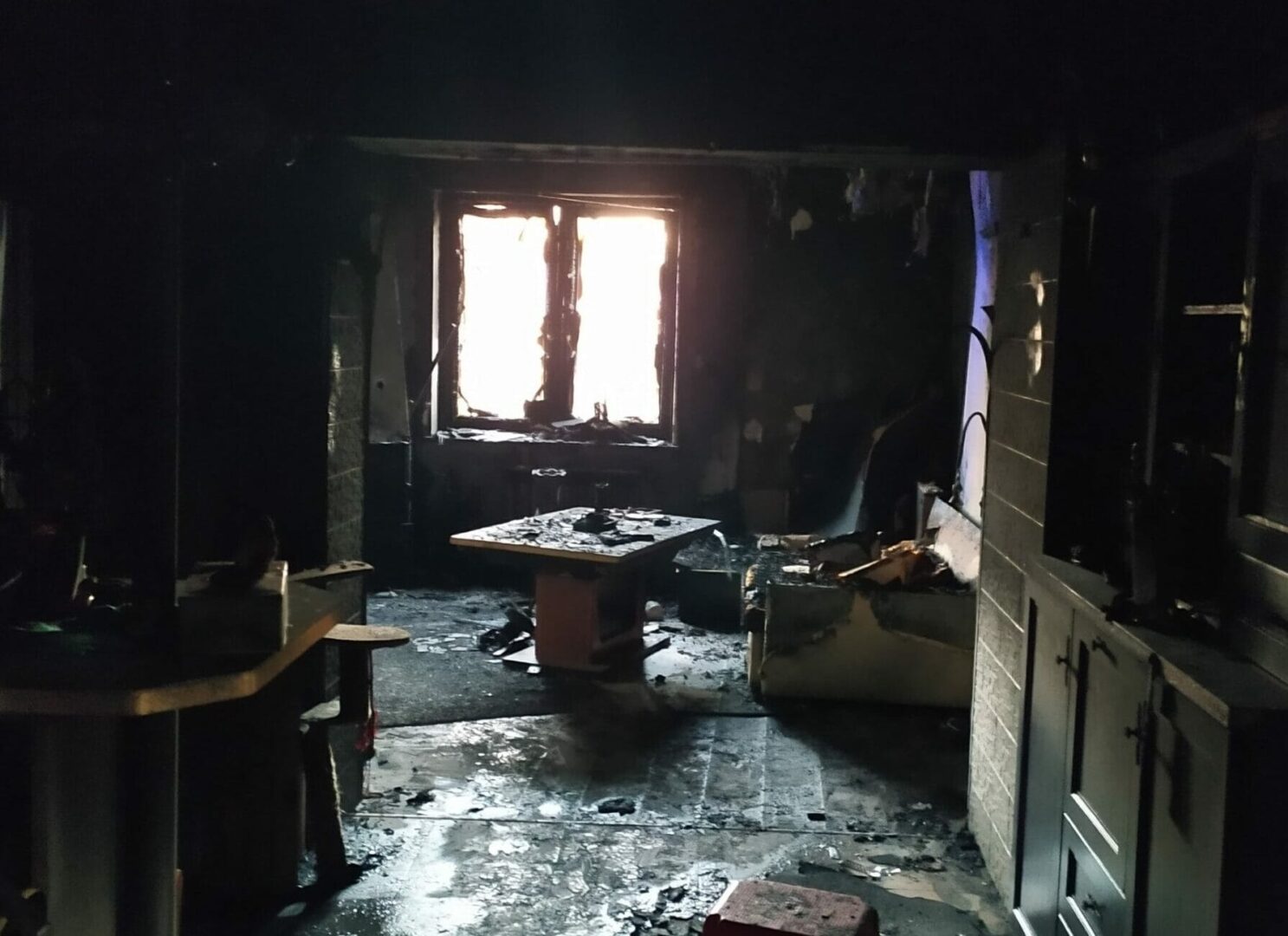 Skutki pożaru domu: pokryte sadzą meble i uszkodzone okno.