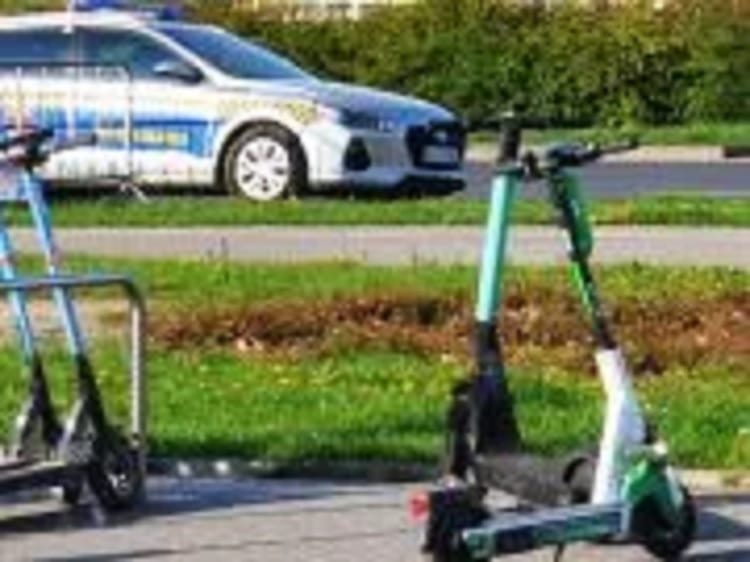 Dwa skutery elektryczne zaparkowane w pobliżu radiowozu.