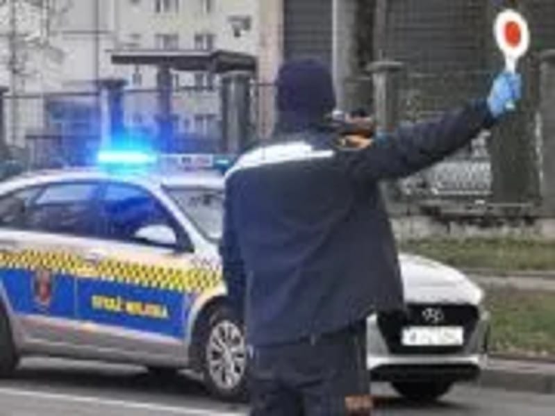 Policjant kieruje ruchem drogowym, ustawiając znak „stop” obok radiowozu.