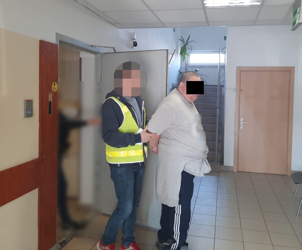 Policjanci zatrzymują podejrzanego na korytarzu budynku.