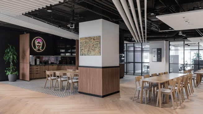 Nowoczesne wnętrze biurowe z drewnianymi stołami i krzesłami oraz dziełami sztuki.