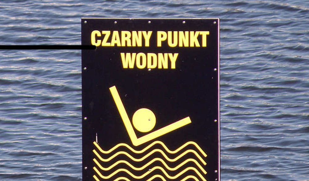 Czarny znak z żółtym tekstem: „Czarny Punkt Wodny”, przedstawiający osobę skaczącą do wody.