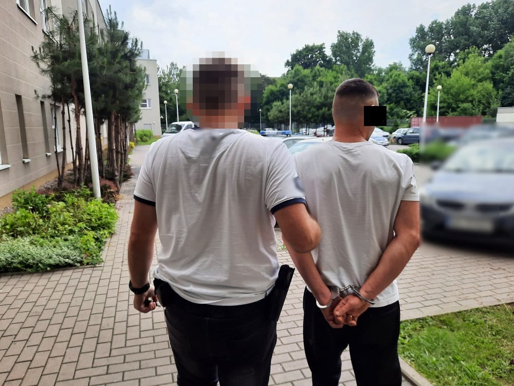 Policjant eskortujący podejrzanego w kajdankach