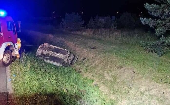 Nocny wypadek samochodowy: przewrócony pojazd obok wozu strażackiego.