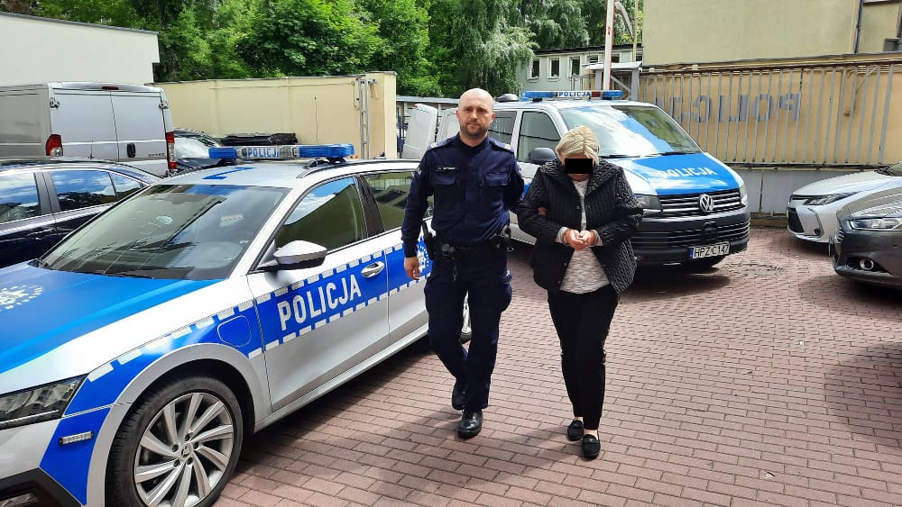 Policjant aresztujący kobietę, widoczne są oznaczone radiowozy POLICJA.