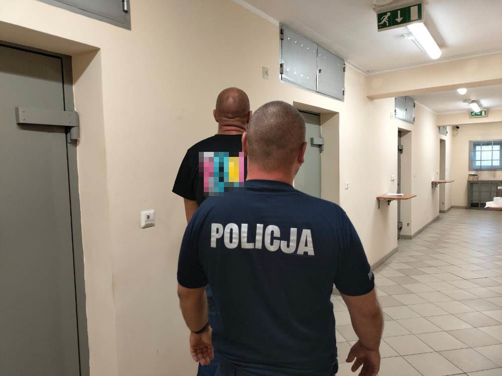 Policjant eskortujący podejrzanego korytarzem więziennym. POLICJA