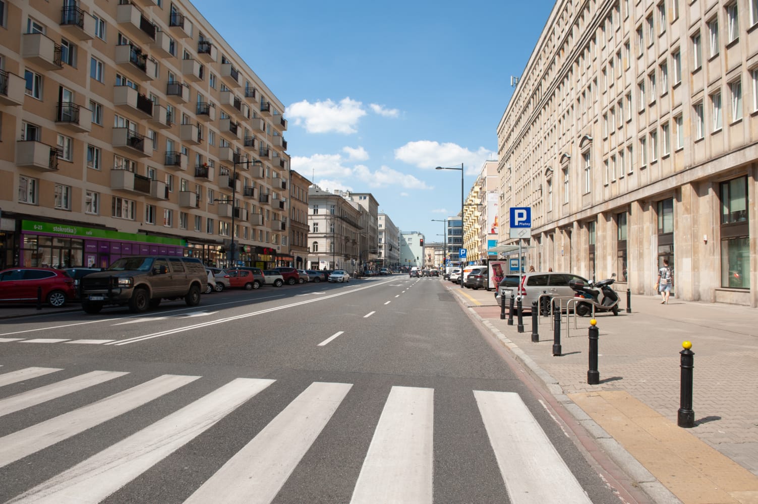 Pusta ulica miejska w Warszawie, z zaparkowanymi samochodami i budynkami mieszkalnymi.