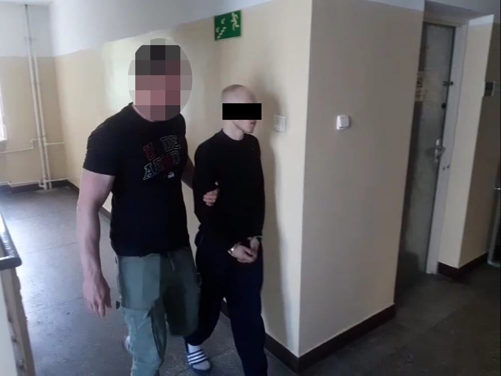 Dwóch mężczyzn w kajdankach, jeden w czarnej koszuli, drugi w ciemnej koszuli i spodniach.