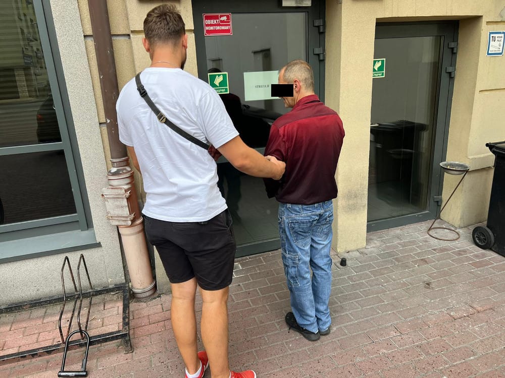 Dwóch mężczyzn stoi przed budynkiem. Jeden z nich wydaje się pomagać drugiemu.