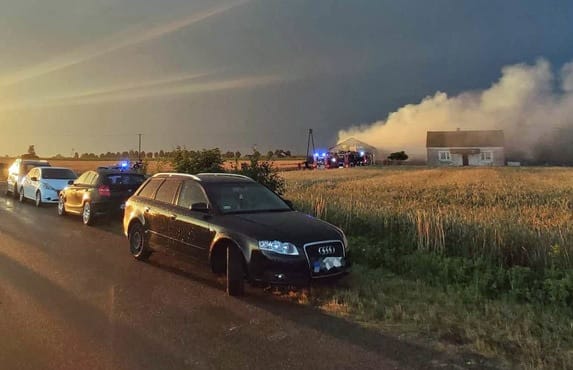 Samochody zaparkowane przy drodze w pobliżu płonącego budynku i strażaków