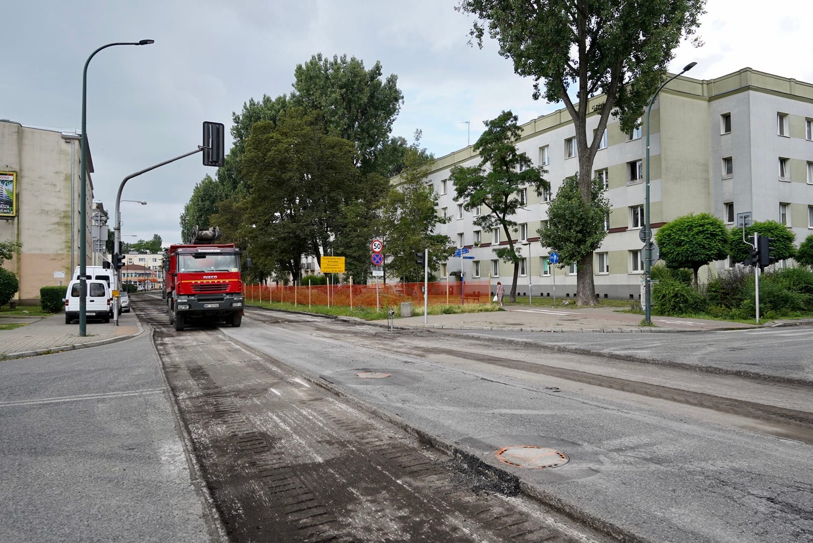 Budowa drogi: Czerwona ciężarówka na świeżo wyasfaltowanej ulicy w pobliżu budynku mieszkalnego.