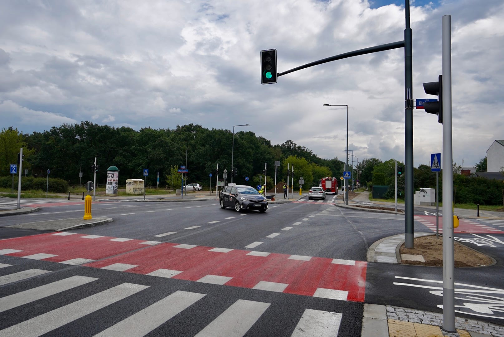 Nowoczesne skrzyżowanie z przejściem dla pieszych i sygnalizacją świetlną; przejeżdża taksówka.