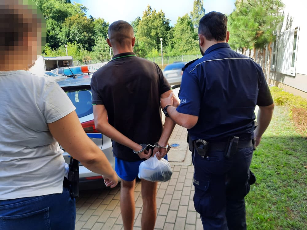 Policjant aresztujący mężczyznę w kajdankach. Kobieta obserwuje w pobliżu.