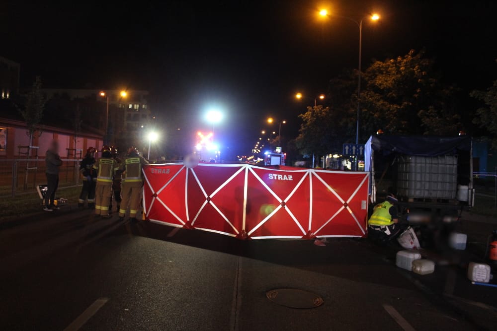 Ratownicy na miejscu wypadku drogowego w nocy. Widoczna bariera „Straż”.