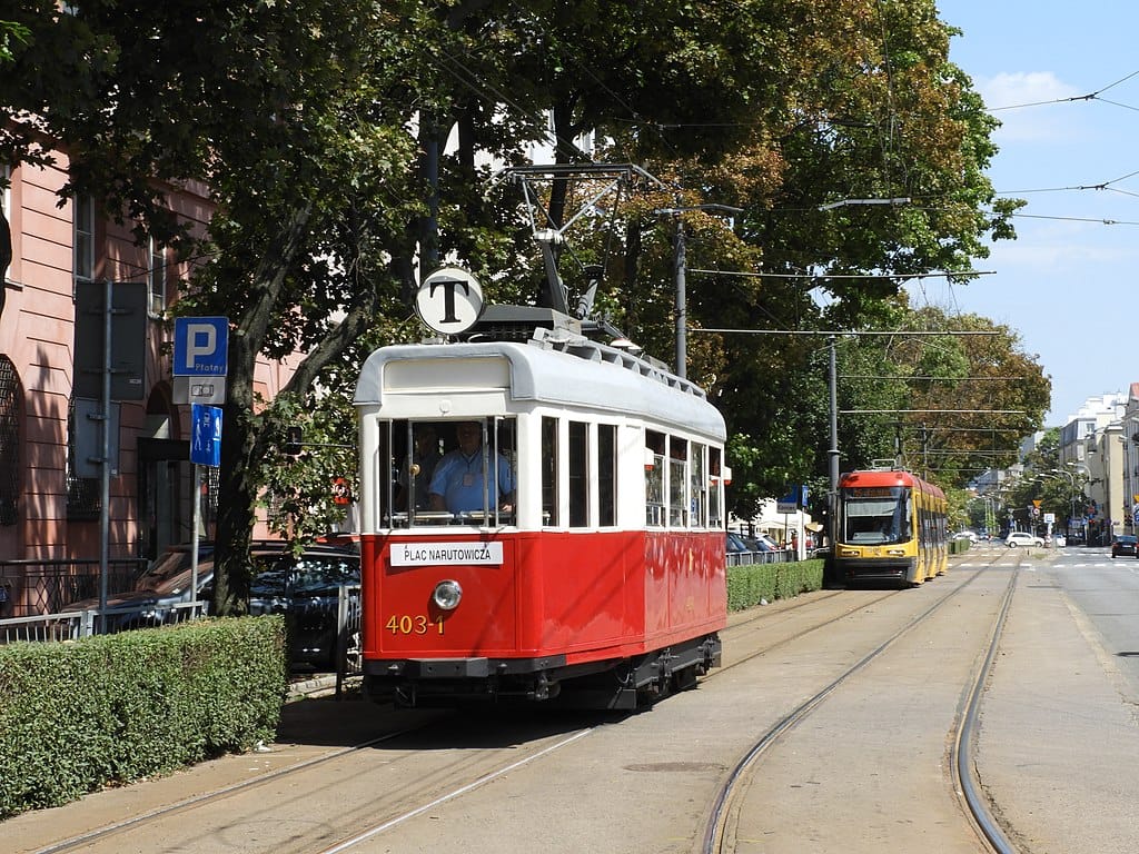 Zabytkowy czerwono-biały tramwaj nr 403-1 na torach miejskich, na tle nowoczesnego żółtego tramwaju.