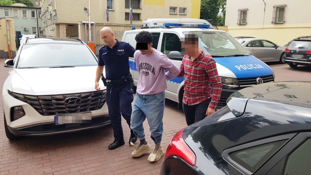 Policjanci zatrzymują dwóch podejrzanych w pobliżu radiowozów.