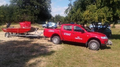 Czerwony wóz strażacki holujący łódź ratowniczą na piaszczystym terenie