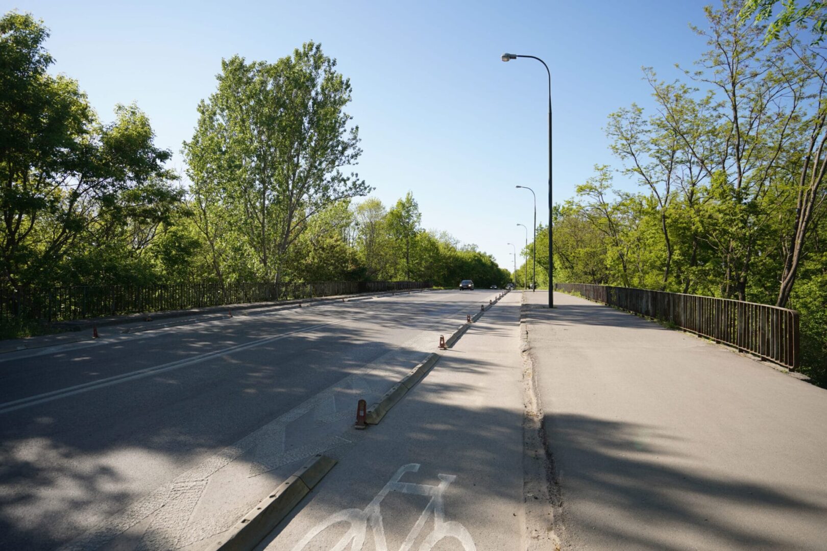 Pusta droga na moście otoczonym drzewami, widoczna ścieżka rowerowa.