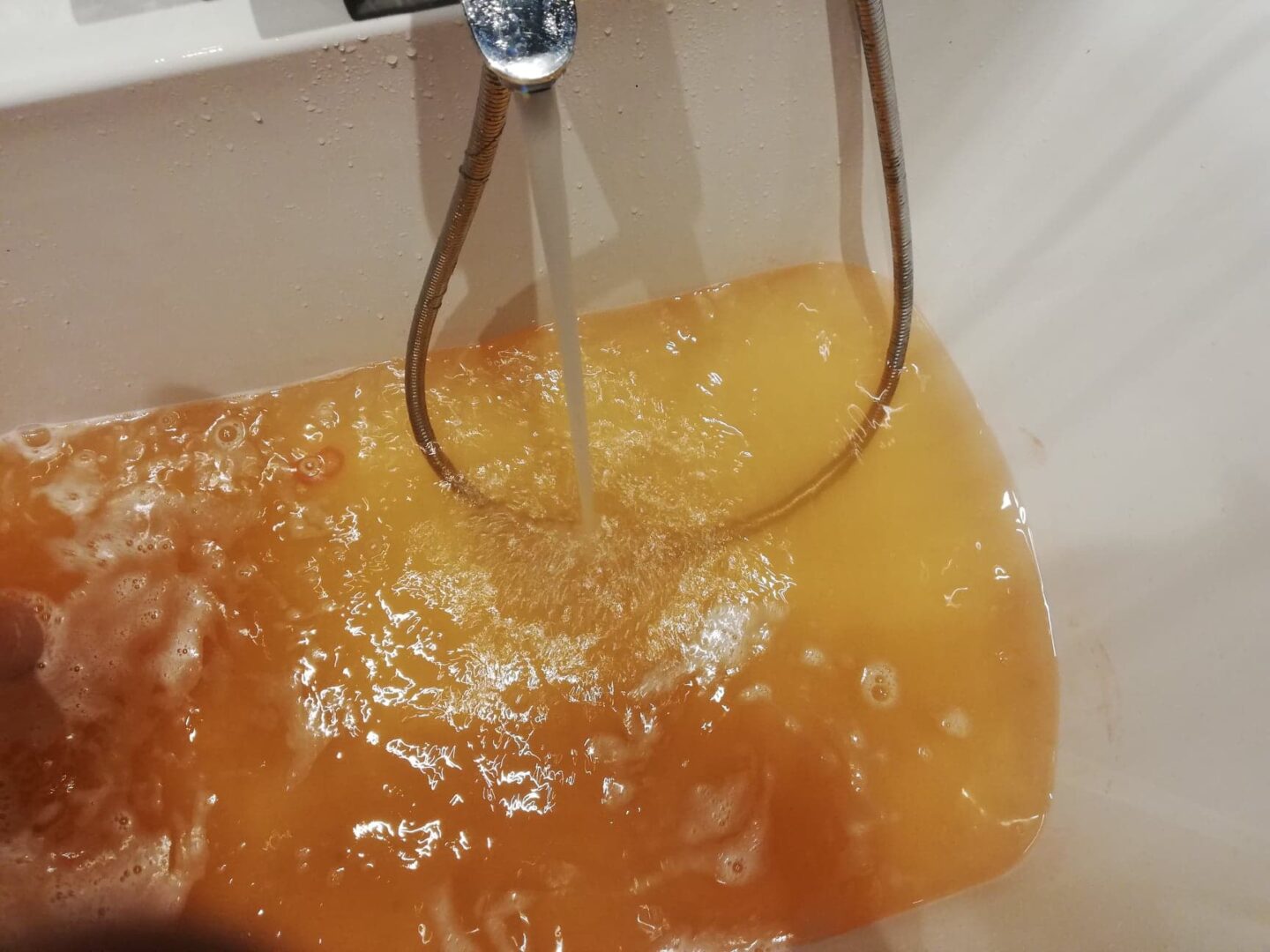 Brązowa woda w wannie wypełnia białą wannę. Woda płynie z chromowanego kranu.