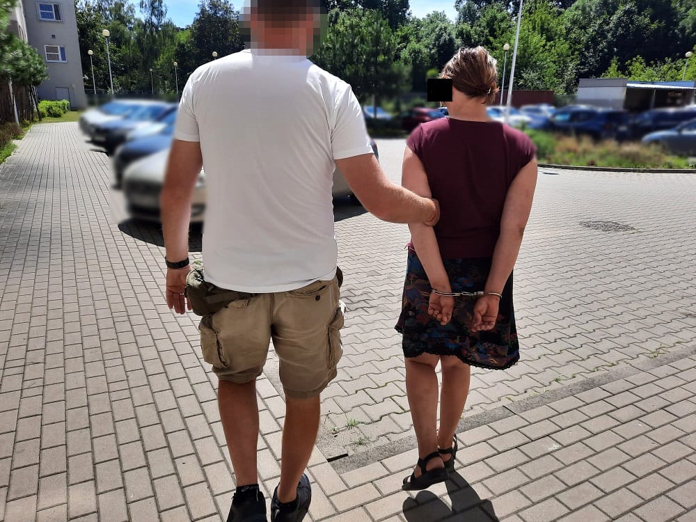 Policjant eskortujący kobietę w kajdankach.