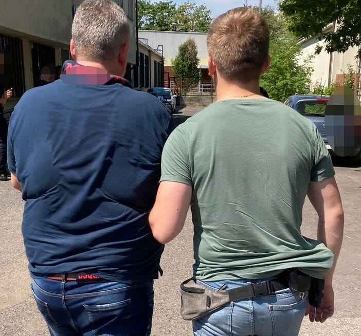 Dwóch mężczyzn w codziennych ubraniach idą razem, prawdopodobnie zostali aresztowani.