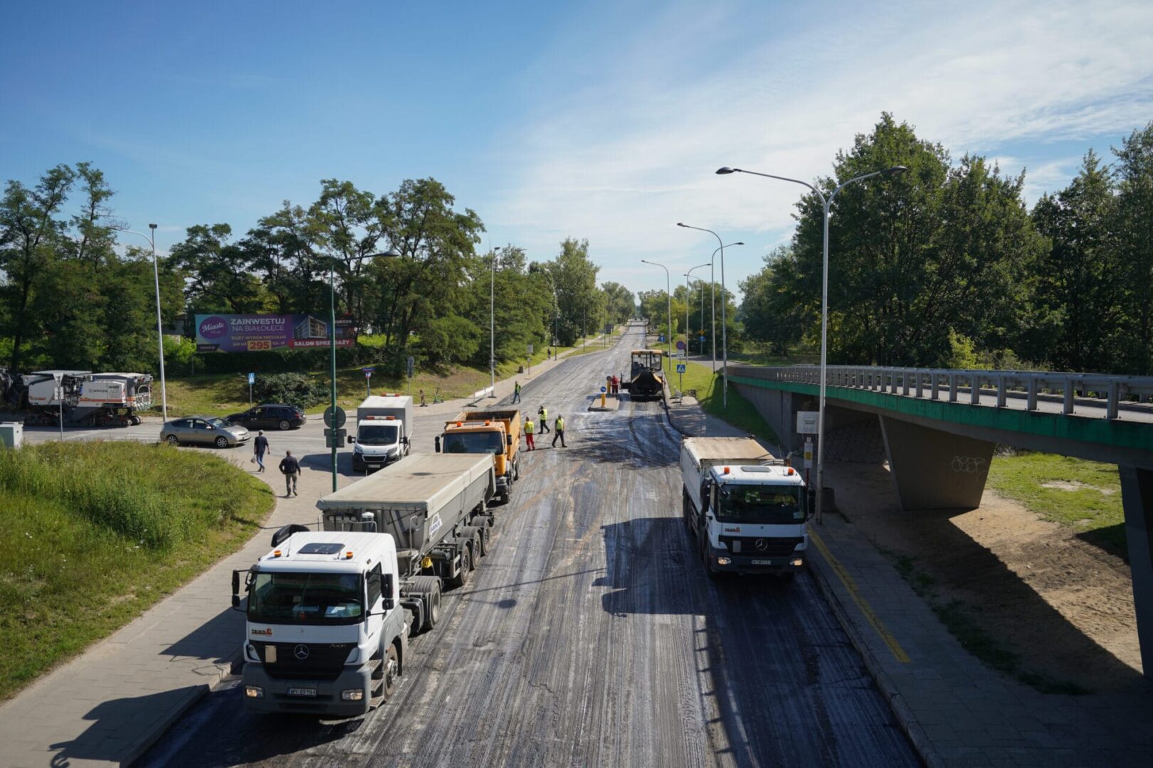 Ekipa drogowa odnawia nawierzchnię ulicy miejskiej, używając ciężarówek i sprzętu.