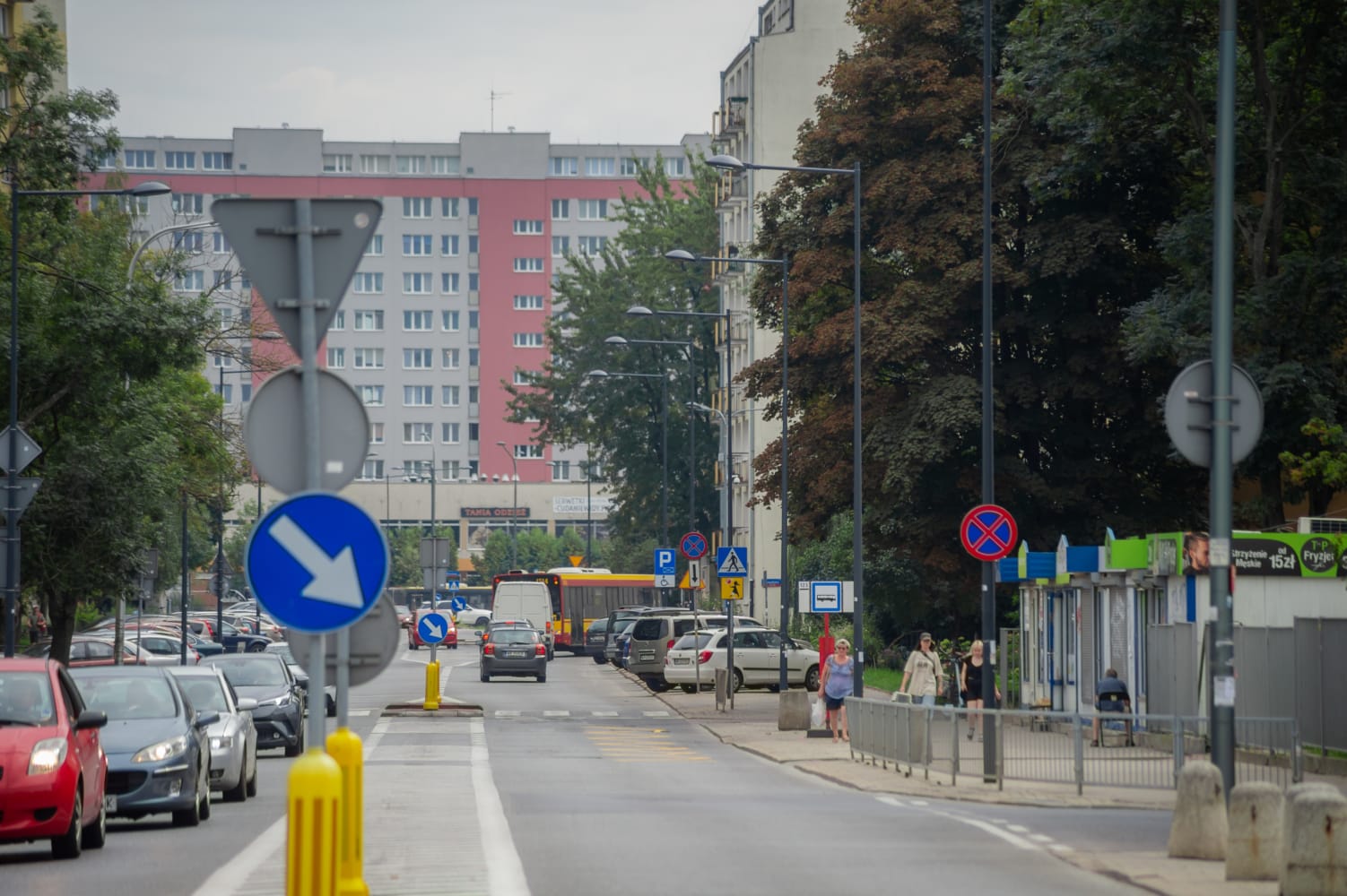 Scena uliczna miasta z samochodami, autobusami i pieszymi w pobliżu budynków mieszkalnych.
