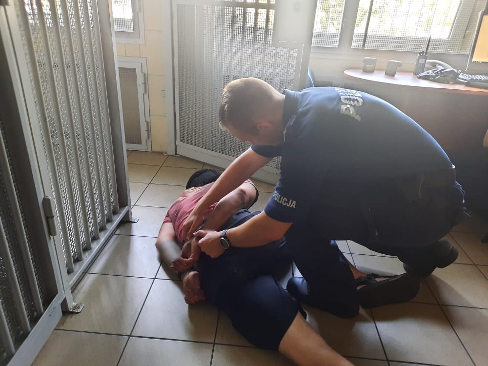 Policjant zakładający podejrzanemu kajdanki na podłodze