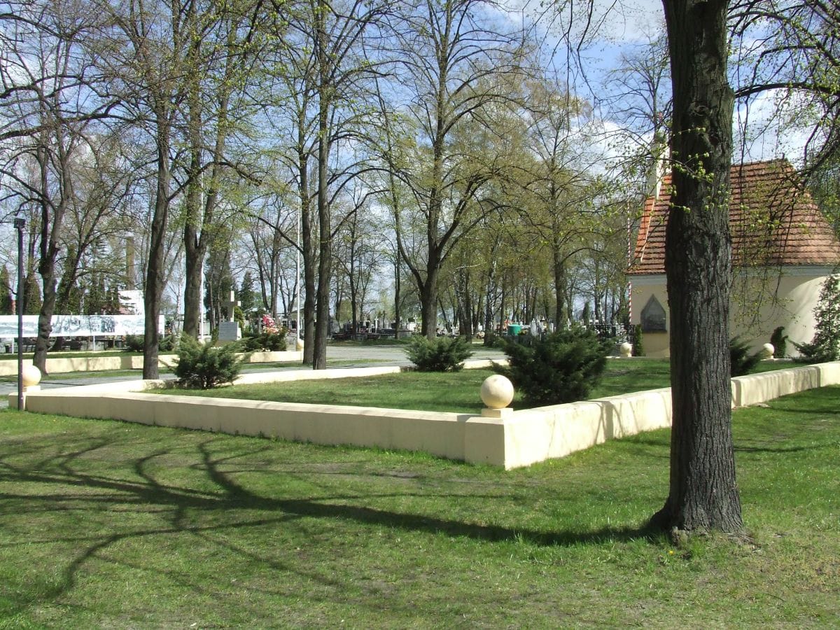 Spokojny ogród cmentarny z małą kaplicą i zadbanymi żywopłotami.