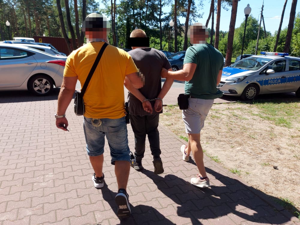 Policja eskortuje podejrzanego w kajdankach
