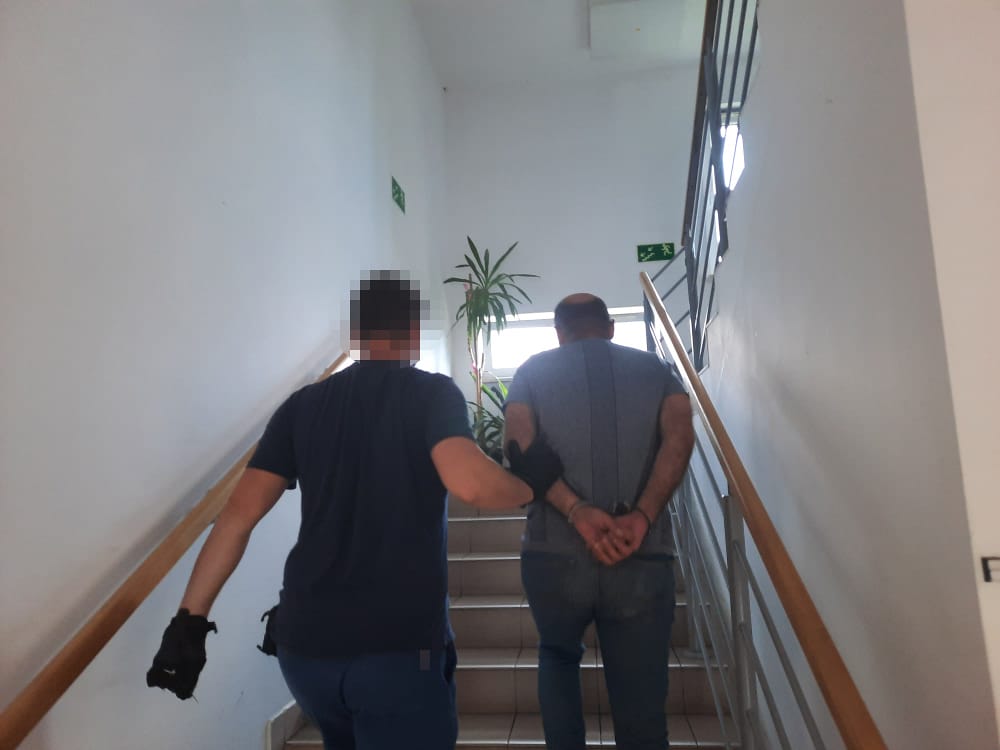 Policjant eskortujący podejrzanego po klatce schodowej.