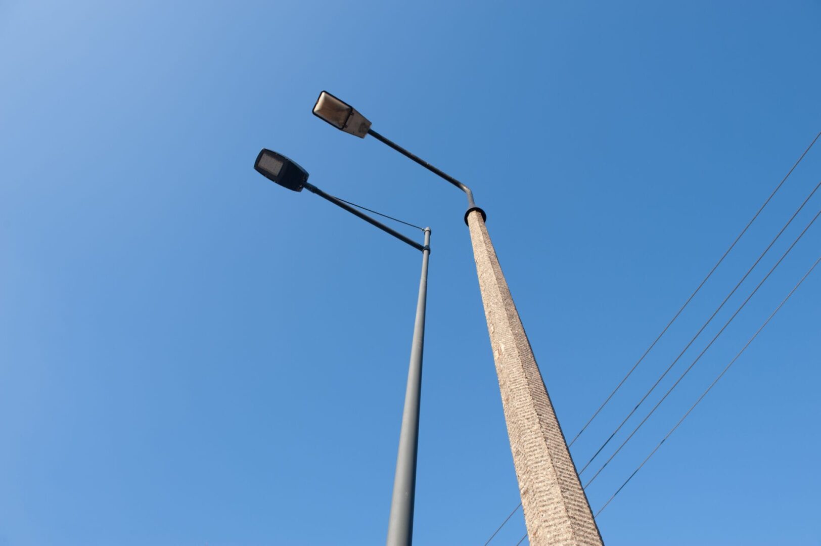 Podwójne latarnie uliczne LED zamontowane na wysokim betonowym słupie na tle czystego, błękitnego nieba.