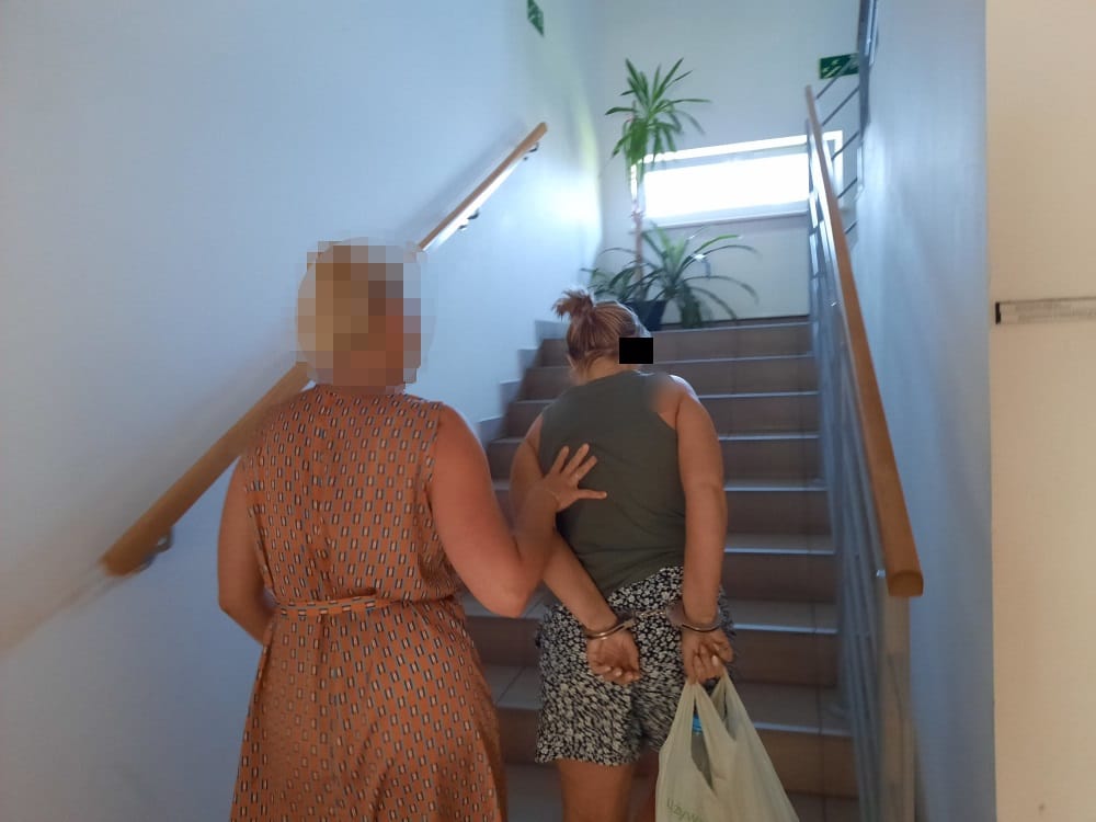 Kobieta w kajdankach eskortowana po schodach przez inną kobietę.