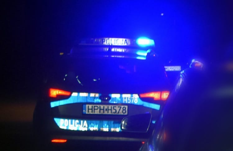 Tylny widok polskiego radiowozu nocą z włączonymi światłami, tablica rejestracyjna HPH H578