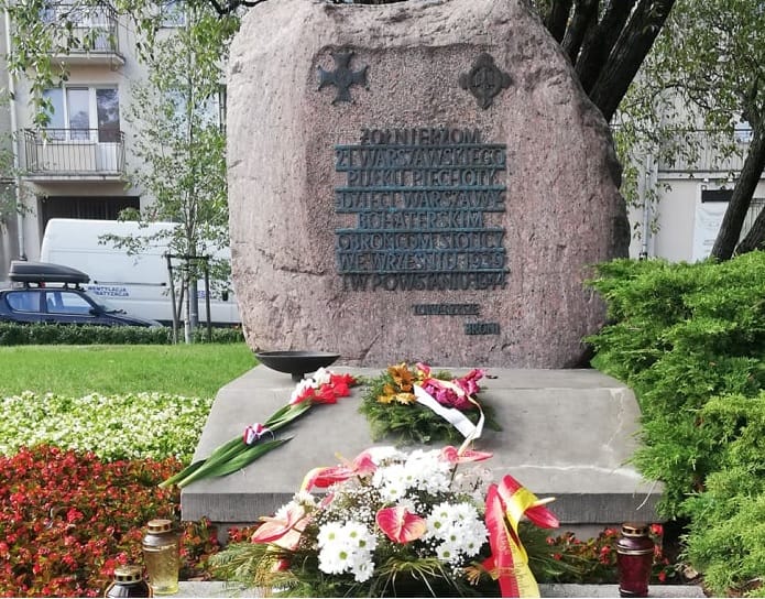 Kamień upamiętniający Powstanie Warszawskie z kwiatami i zniczami