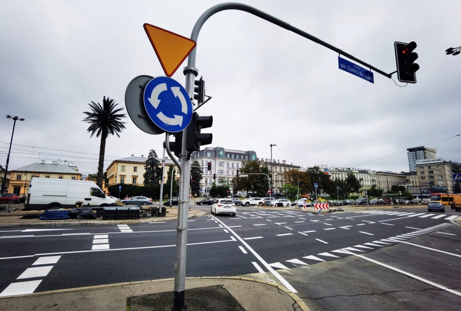 Skrzyżowanie o ruchu rondowym ze znakami drogowymi i sygnalizacją świetlną.