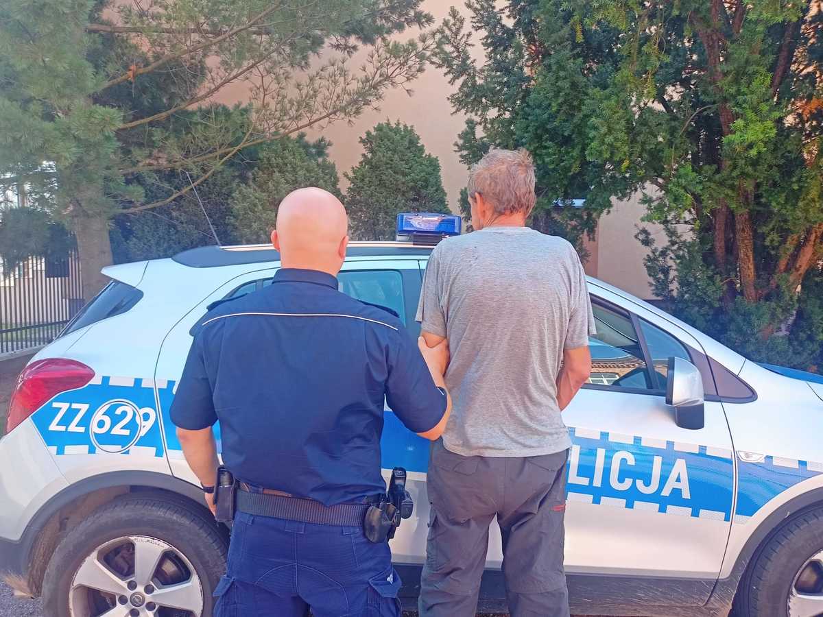 Policjant aresztujący mężczyznę obok radiowozu. Na radiowozie widnieje napis „LICJA”.