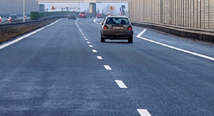 Pusta autostrada z jadącym samochodem, widocznymi oznakowaniami drogi i ekranem dźwiękochłonnym.