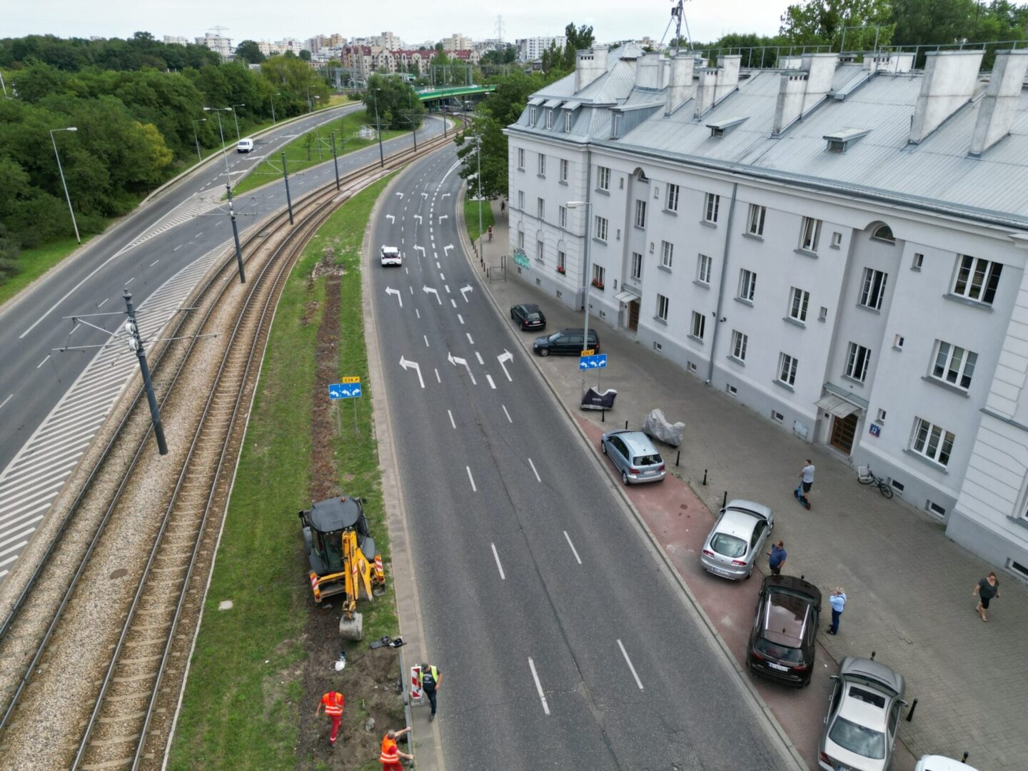 Widok z lotu ptaka na trwającą w pobliżu budynku budowę drogi. Obecni są pracownicy i maszyny.